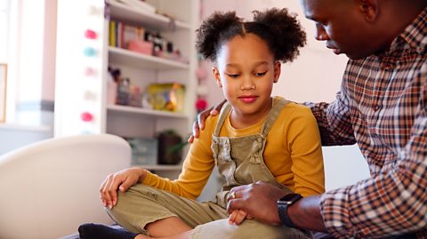 Dad comforts young girl 7-8 years of age on bed in her bedroom