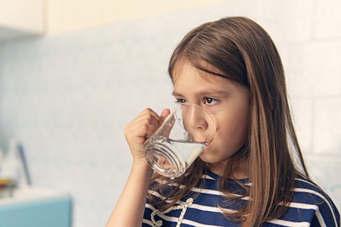 Little girl drinks from a glass mug of water in a family kitchen