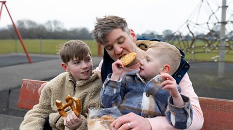 Dad and two sons in the park eating and chatting