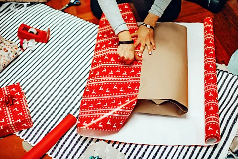 Getty Images A person trying to pull red festive wrapping paper over an awkwardly shaped gift (Credit: Getty Images)