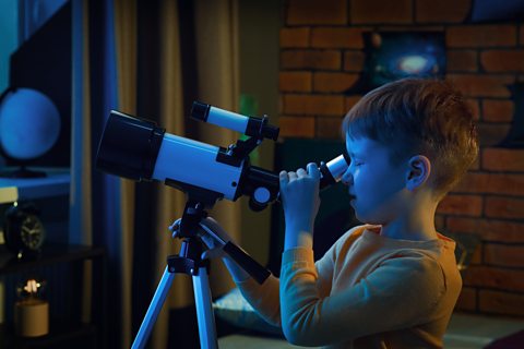 Little boy looking at stars through a telescope in a room