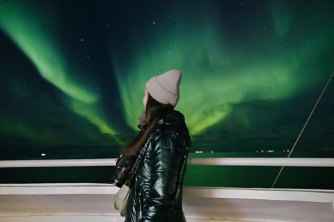 Side view of female traveller overlooking dramatic bright Aurora in the sky while crossing the ocean by the ship in northern Norway