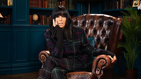 Claudia Winkleman sitting on a chair.