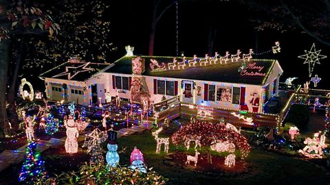 Single-story house decorated with elaborate Christmas lights and holiday figures, including reindeer, Santa’s sleigh on the roof, glowing snowmen, and a large illuminated star in the yard.