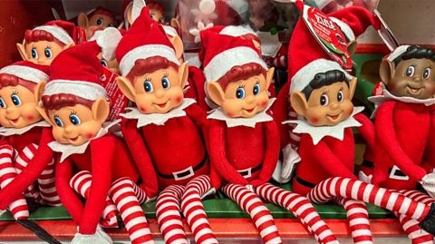 A shelf full of toy elves dressed in red and white striped leggings, red tops and pointy hats