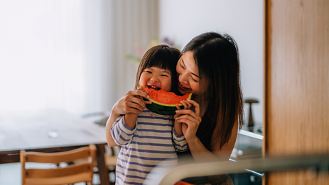 A young girl and her mum enjoy a big slice of watermelon.