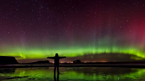 Silhouette of woman standing on Seacliff Beach in Scotland, East Lothian, watching Northern lights - stock photo