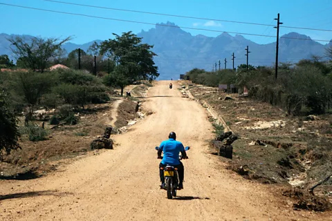 Kang-Chun Cheng A man on a motorbike riding down a dirt track stretching towards mountains in the distance (Credit: Kang-Chun Cheng)