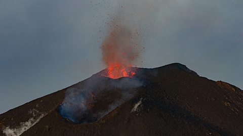 A close up of Mount Etna in Italy as it erupts and orange lava spurts out from the top
