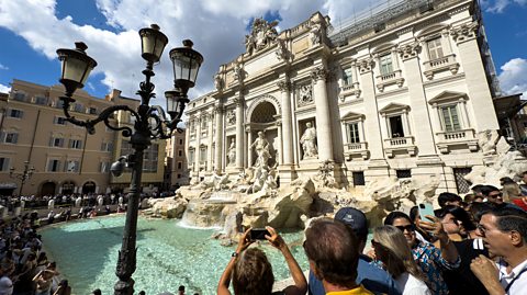 Tourists gather around and take photos of the Trevi Fountain in Rome, a grand Baroque fountain made of white stone