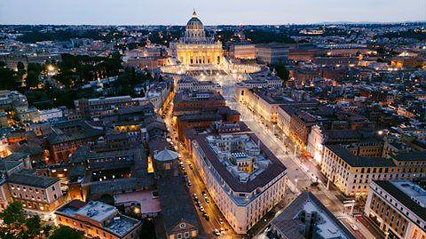 St Peter's Basilica and Vatican city at dusk . The aerial shot shows the buildings around the city lit up at the domed church, St Peter's Basilica, at the top