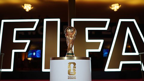 The Fifa World Cup trophy on a plinth with a large Fifa logo behind it