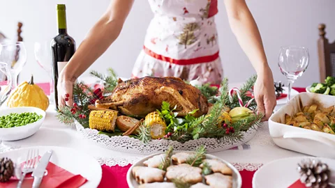 Getty Images A woman holding platter of food above Christmas meal (Credit: Getty Images)