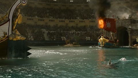 A flooded Colloseum with a shark and two naval ships in it.