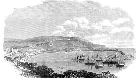 Vintage engraved illustration of a coastal harbor scene with sailing ships anchored near a curved pier, surrounded by seaside buildings and rolling hills under a partly cloudy sky.
