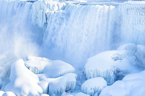 A white and crystal blue waterfall cascades over ice formations