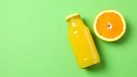 Getty Images A bottle of orange juice and half an orange on a green background (Credit: Getty Images)