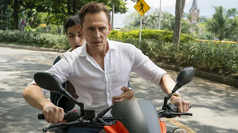 BBC Tom Hiddleston riding a motorcycle with a young boy sat behind him in The Night Manager season two (Credit: BBC)
