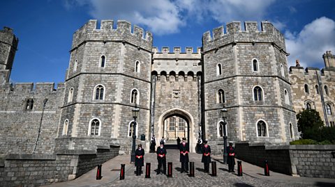 Pesë anëtarë të stafit të veshur me uniforma të zeza qëndrojnë jashtë hyrjes së Kështjellës Windsor