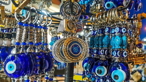 A shop in Greece selling keyrings with different evil eye designs, all hanging on display. The symbol is a blue gem with a white circle, blue contact and black pupil representing the eye