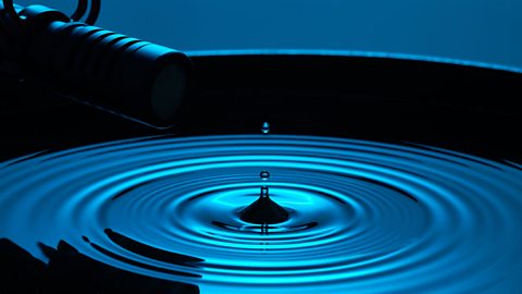 A microphone records the precise sound of a water drop creating ripples with cinematic blue lighting