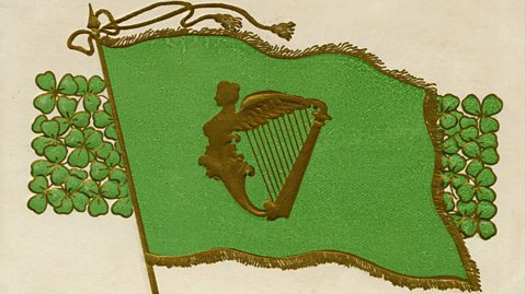An illustration of a green flag with gold trimming and a gold Celtic harp, a symbol of Ireland. Behind the flag is a rectangle full of shamrocks, three-leaved green plants which are also a symbol of Ireland