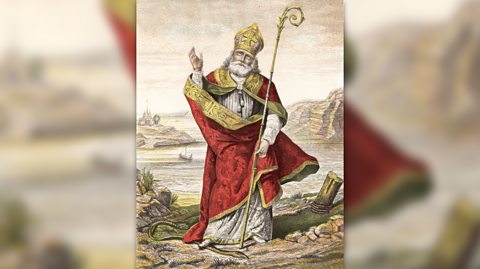 An illustration of St Patrick, patron saint of Northern Ireland, with a sceptre and wearing a red and gold cloak, standing on a snake as he gestures to the sky