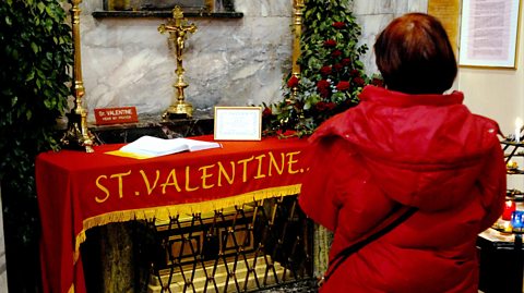 A woman in a red waterproof coat pays tribute to the statue of patron saint of love, St. Valentine, inside Whitefriar Church in Dublin. Around it is a red and yellow cloth reading St Valentine