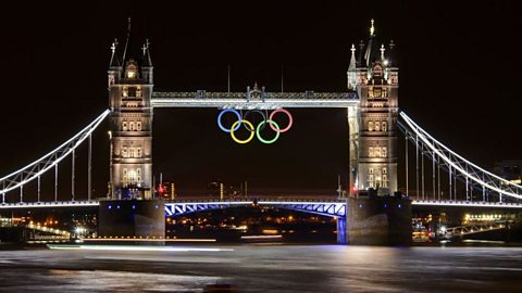 Tower Bridge in London illuminated at night with Olympic rings displayed between its towers, reflecting on the River Thames during the Olympic Games celebration.