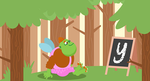 Hairy fairy wearing a pink tutu sat in front of a blackboard.