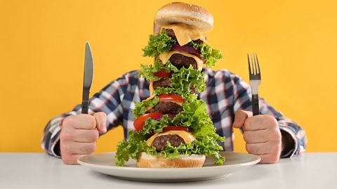 Image of a man holding a knife and fork about to tuck into a burger with five patties