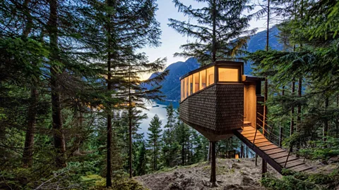 Exterior of a modern tree house in a forest overlooking a lake and mountains (Credit: Woodnest/ Sindre Ellingsen)