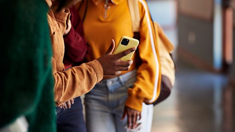 Close-up of people standing together indoors, one person holding a yellow smartphone, wearing casual jackets and jeans