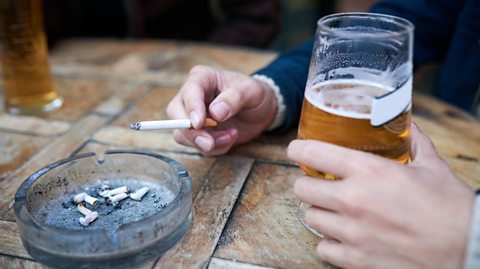 Cropped shot of an unrecognisable man smoking and drinking a glass of beer at a bar.
