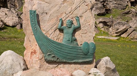 A beige stone monument in Greenland to Erik the Red shows the viking in a longboat with a beard and his arms above his head. The figure is the colour teal 