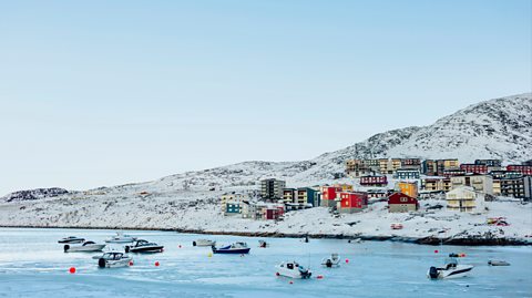 Colourful houses on the snowy land in Greenland, with boats anchored in the water in front of them