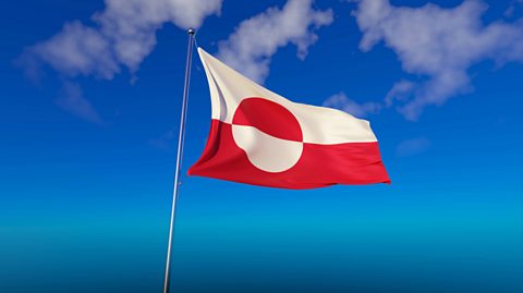 The Greenland flag blowing on a pole in the wind. It is half white and half red (the rectangles on top of one another) with a circle in the centre. The circle in the centre is half red and white, contrasting the background of the flag whose colours are in reverse