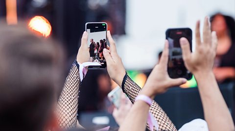 Close-up of two pairs of hands in a crowd holding smart phones. They are filming live on their phones