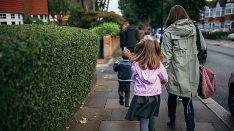 A mother and daughter walking along a suburban street, seen from behind.