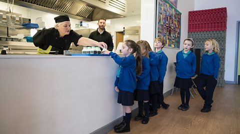 Primary school children queuing for milk from lunch lady in the canteen.