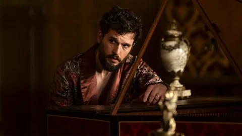 HBO Kit Harington sat at a grand piano wearing a silk dressing gown in Industry season 4 (Credit: HBO)