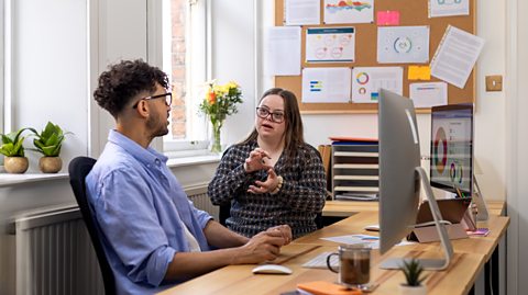 Male and female colleagues working at a desk with two computer screens.