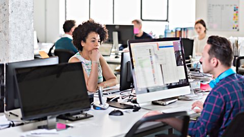 A woman and a man working on desktop computers at a desk in a modern office.
