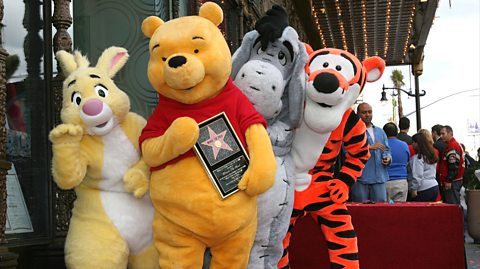 Disney's Rabbit, Winnie The Pooh, Eeyore and Tigger pose for photos as Winnie The Pooh receives a star on the Hollywood Walk of Fame. They are people in lifesize costumes of the characters. Rabbit is yellow with a white stomach, Pooh is a yellow bear with a red top holding the award, Eeyore is a grey donkey and Tigger is an orange and black striped tiger