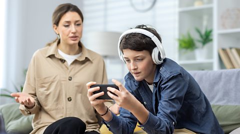 Woman looks at a young boy on his device with headphones 