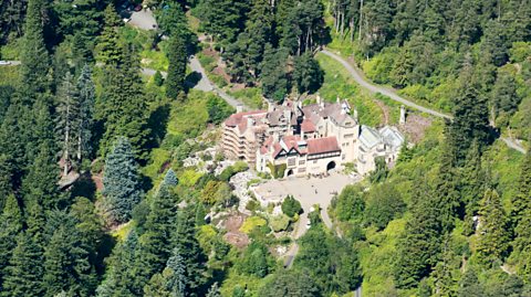 Aerial view of Cragwood estate. Surrounded by greenery and tall trees of different shades of green, at the centre is a stately home with a large front drive. It is grand with cream walls and orange slates on the roof