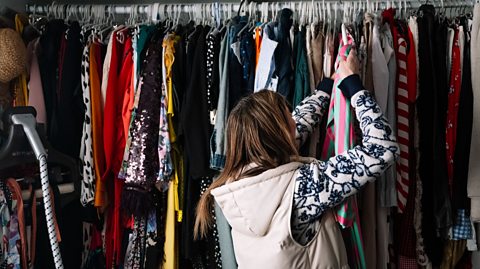 Women in a gilet in a room examining a large and overflowing wardrobe of clothes.