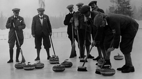 A black and white photo of the 1924 British curling team, dressed in their formal playing uniforms, stood on the ice