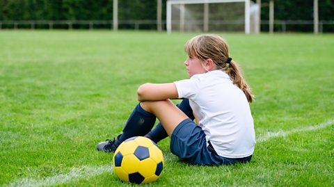 Young girl sits on a grass pitch next to a football