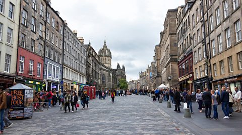 Edinburgh's Royal Mile, full of shoppers walking through the old town. Each side of the street is lined with old buildings and various shops and businesses